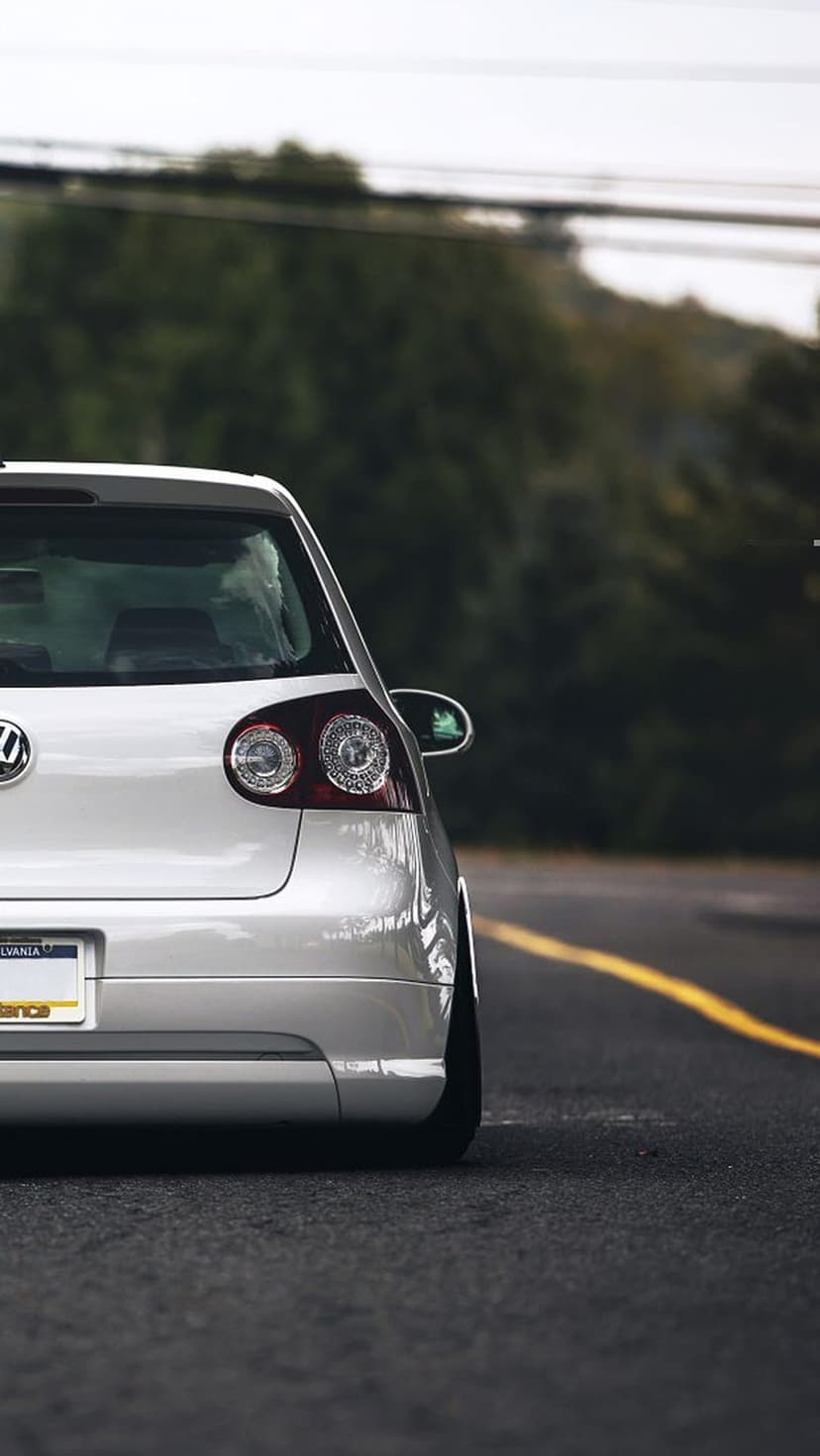 White Volkswagen Golf R rear view on an asphalt road with yellow lines and a lush green forest background.