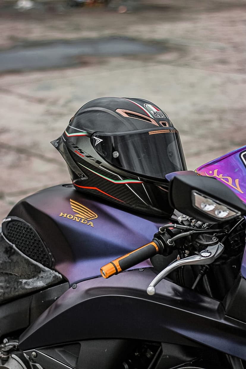 Black racing helmet with Italian flag accents resting on an iridescent purple Honda motorcycle fuel tank.