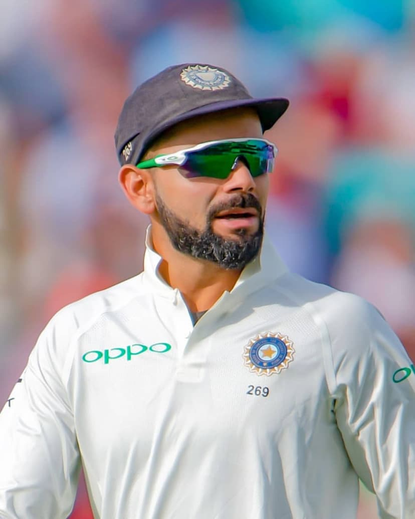 Virat Kohli in white Test cricket uniform with sunglasses and a team cap, looking sideways in a close-up shot.