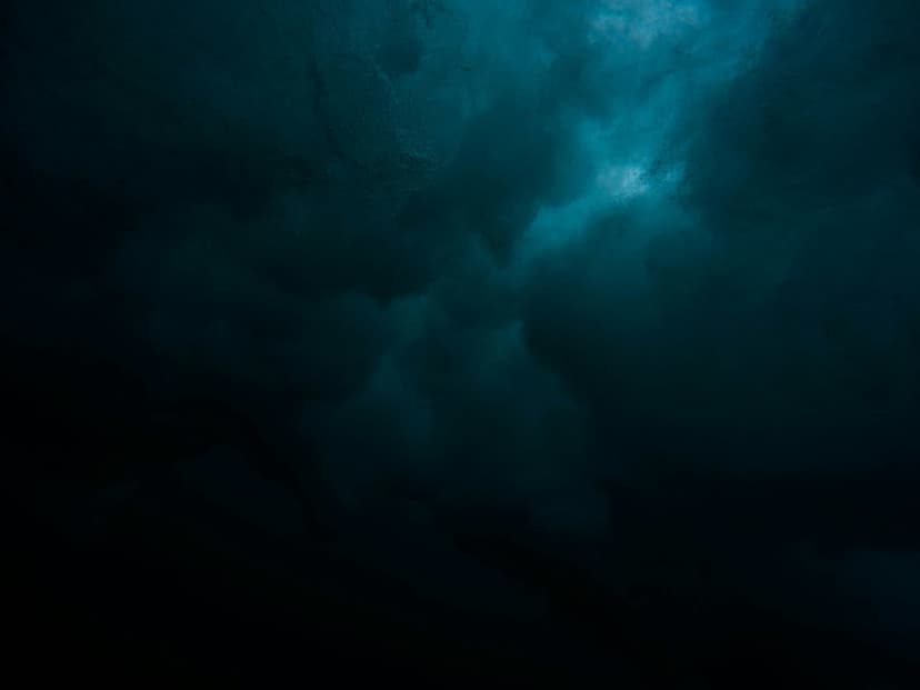 Dark teal and black clouds swirling around a bright point of light breaking through from the upper right corner.