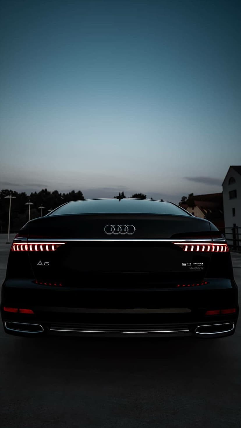 Black Audi A6 rear view at twilight showing illuminated LED taillights and chrome badges on the trunk lid.
