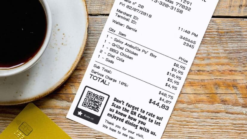 White coffee cup and a paper receipt rest on a dark wooden table next to a corner of a yellow card.