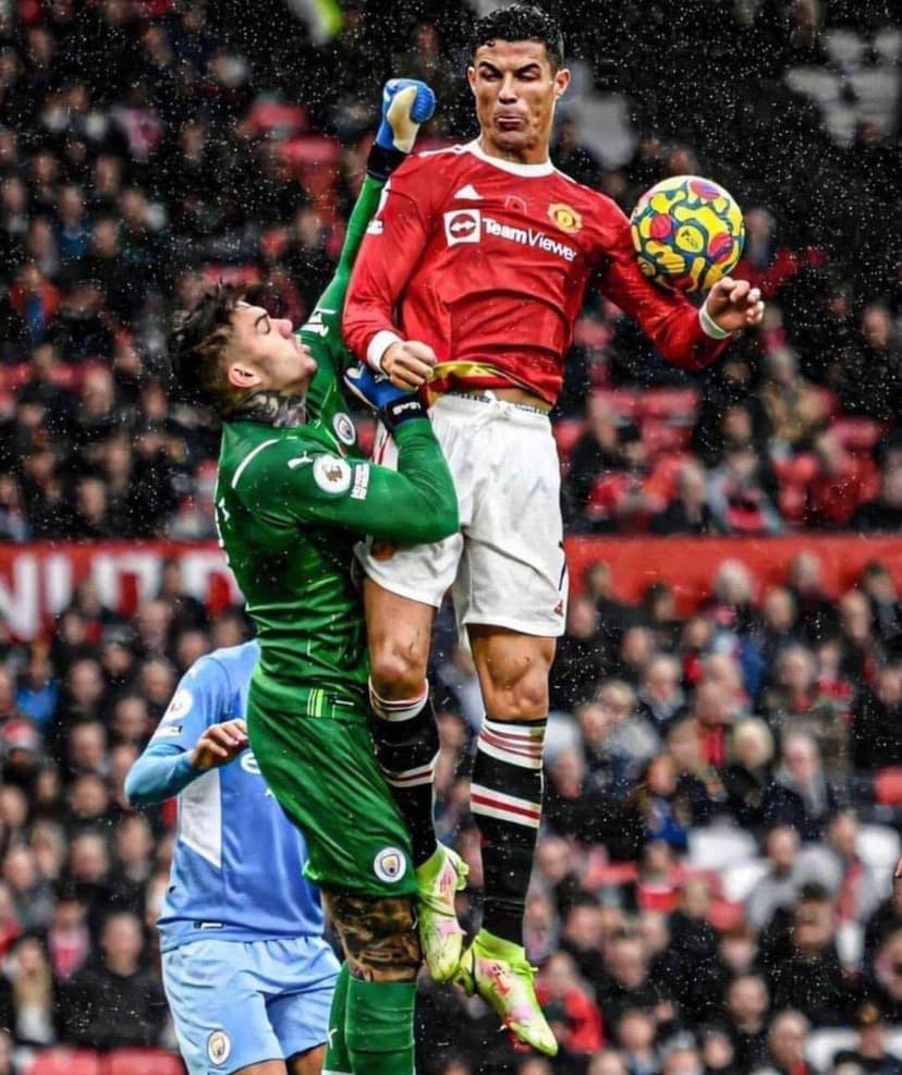 Cristiano Ronaldo and Ederson Moraes leap for a football during a competitive Manchester derby match at Old Trafford.