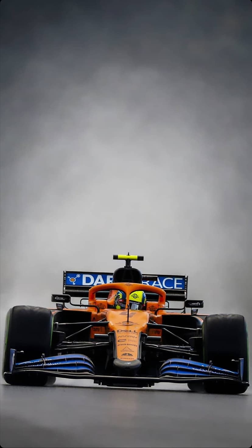 McLaren Formula One car with orange livery and a driver in the cockpit against a misty grey background.