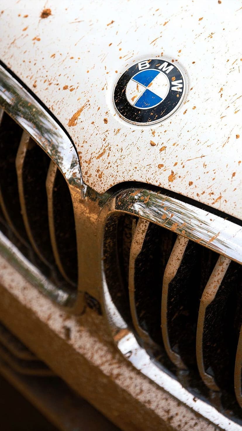 BMW logo and white car hood with brown mud splatters capture the essence of a rugged off-road drive.