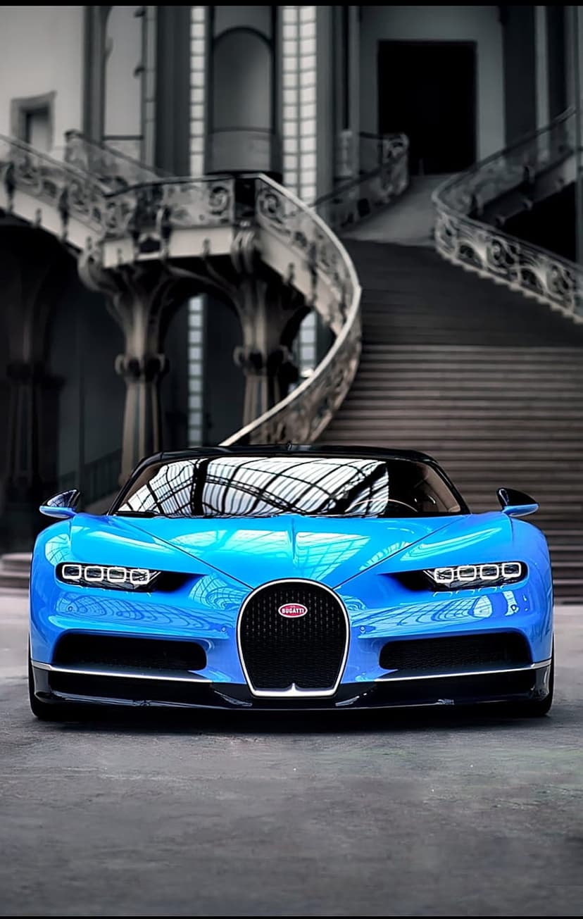Blue Bugatti Chiron hypercar parked inside a grand hall featuring a large spiral staircase in the background.