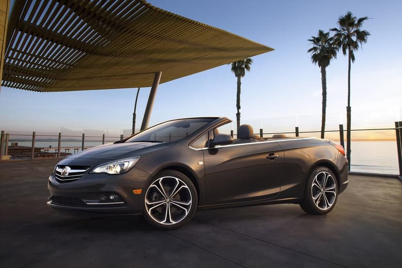 Dark grey convertible parked under a wooden canopy by the ocean at sunset with palm trees and soft golden light.