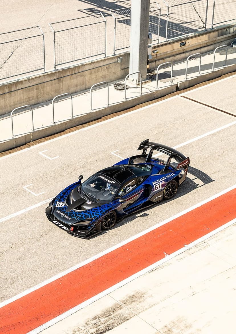 McLaren Senna GTR racing car with blue geometric patterns and number 67 on a paved track with orange strips.