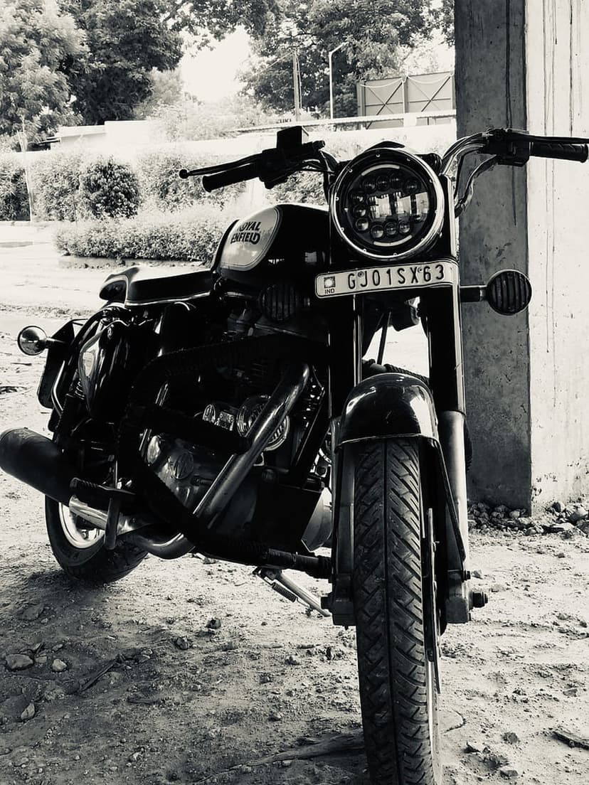 Royal Enfield Classic motorcycle with chrome accents parked on dirt ground in a monochrome outdoor setting.
