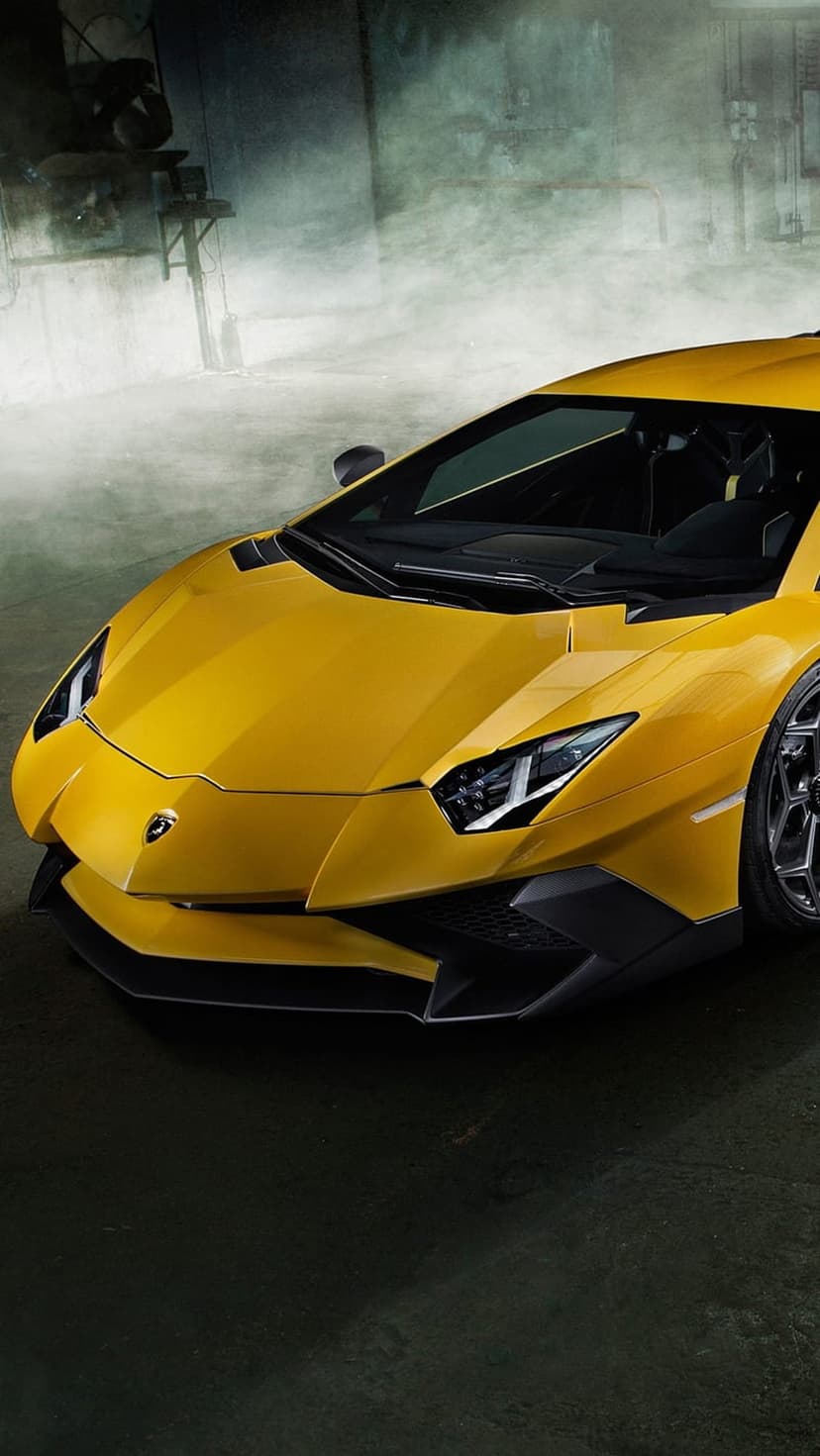 Yellow Lamborghini Aventador with glowing LED headlights and sharp front vents against a dark industrial floor.