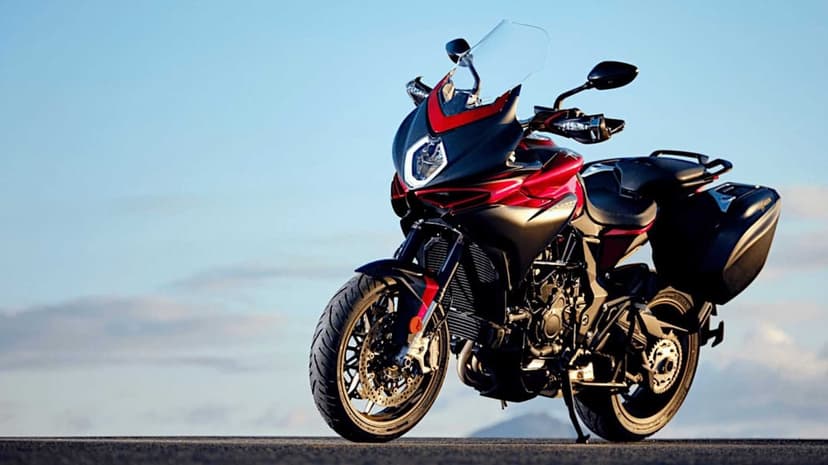 Red and black MV Agusta motorcycle with side luggage parked on an open road under a clear morning sky.