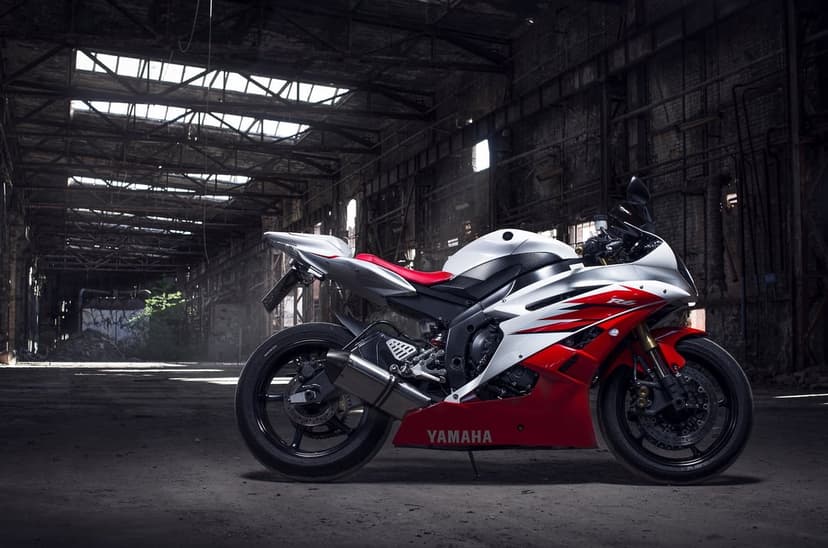 White and red Yamaha R6 sportbike parked inside a dark, gritty industrial warehouse with light from skylights.