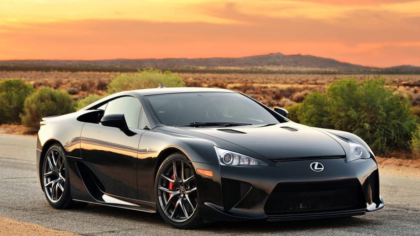 Black Lexus LFA supercar parked on a desert road under a vibrant orange sunset sky with mountain silhouettes.