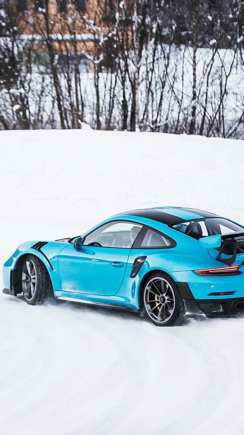 Blue Porsche 911 GT2 RS drifting on a snowy road with ice particles flying behind the rear wheels during winter.