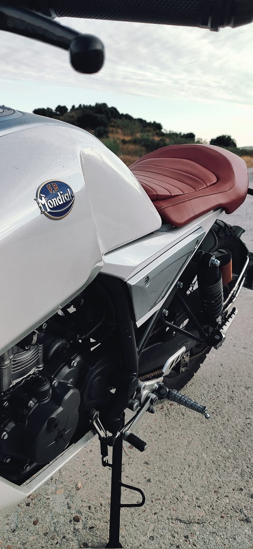 Custom Mondial motorcycle with a red leather seat and white fuel tank parked on pavement against blurred hills.