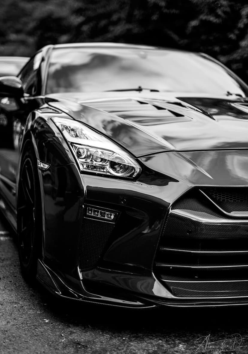 Nissan GT-R front end shows detailed carbon fiber accents and sharp headlights in a black and white close-up.