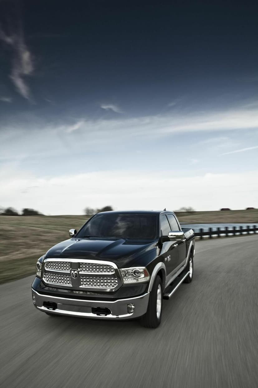 Black Ram pickup truck with chrome accents driving on a paved road under a blue sky with streaky clouds.