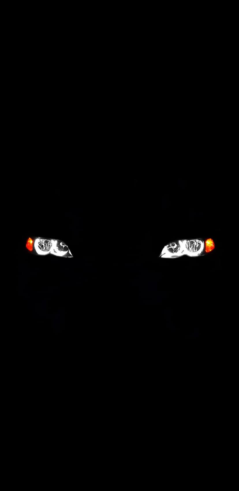 Twin car headlights illuminate the darkness with intense white and amber glows against a deep black background.