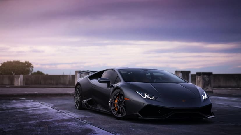 Dark grey Lamborghini Huracán on a concrete rooftop with orange brake calipers under a purple twilight sky.