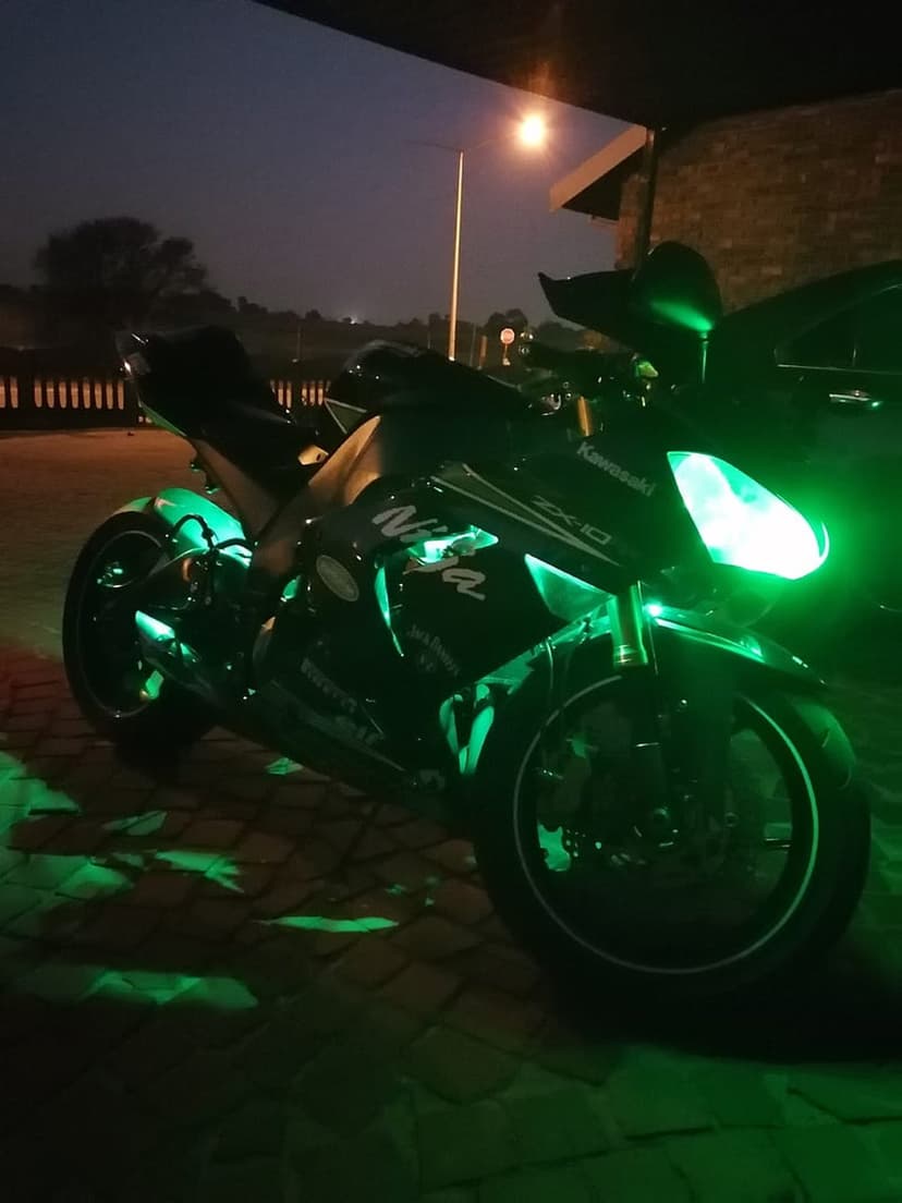Kawasaki Ninja ZX-10R sportbike with neon green LED underglow on a dark asphalt road under night skies.