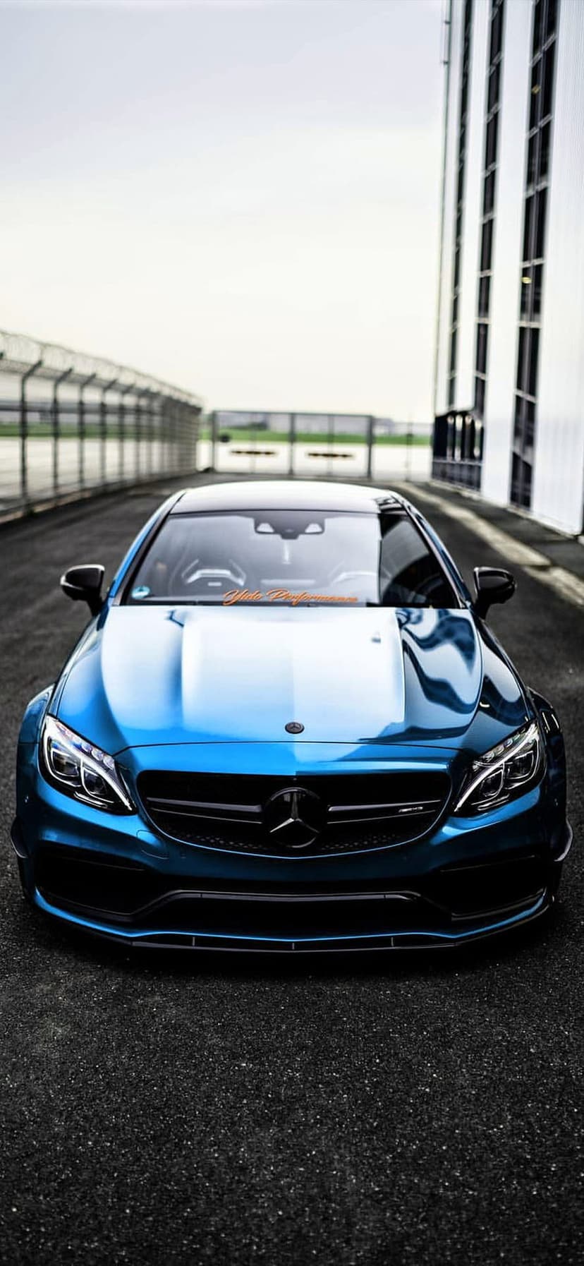 Blue Mercedes-AMG C63 Coupe with aggressive grille and LED headlights parked on a gray asphalt racing circuit.