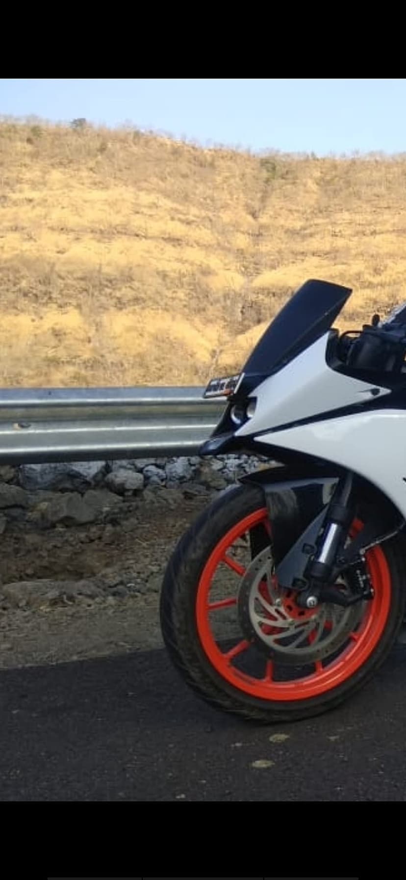 White KTM RC motorcycle front wheel with orange rims and disc brakes on an asphalt road under a blue sky.