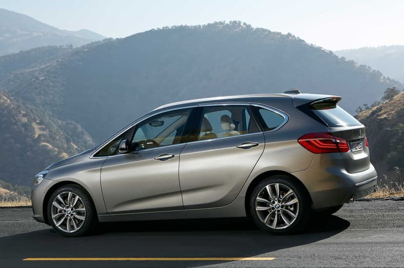 Silver BMW luxury hatchback on an asphalt mountain road with a hazy mountain range in the bright background.