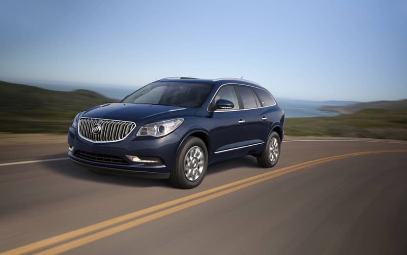 Dark blue Buick Enclave driving on a winding coastal road with ocean views and motion-blurred road lines.