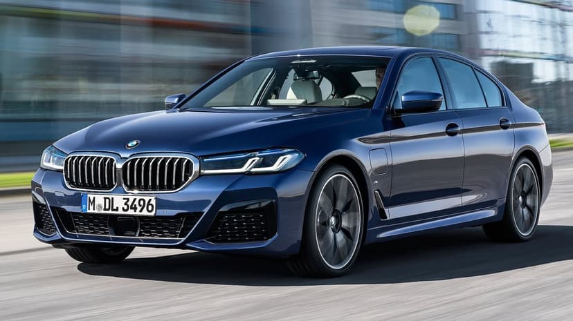 Blue BMW 5 Series sedan driving on a city road with motion blurred wheels and modern architecture background.
