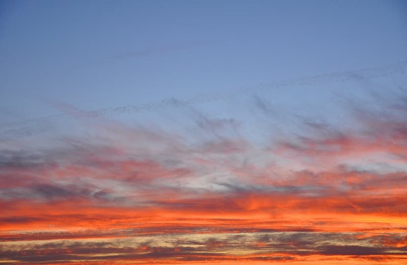 Fiery orange and red cirrus clouds streak across a blue and purple sunset sky during a dramatic golden hour.
