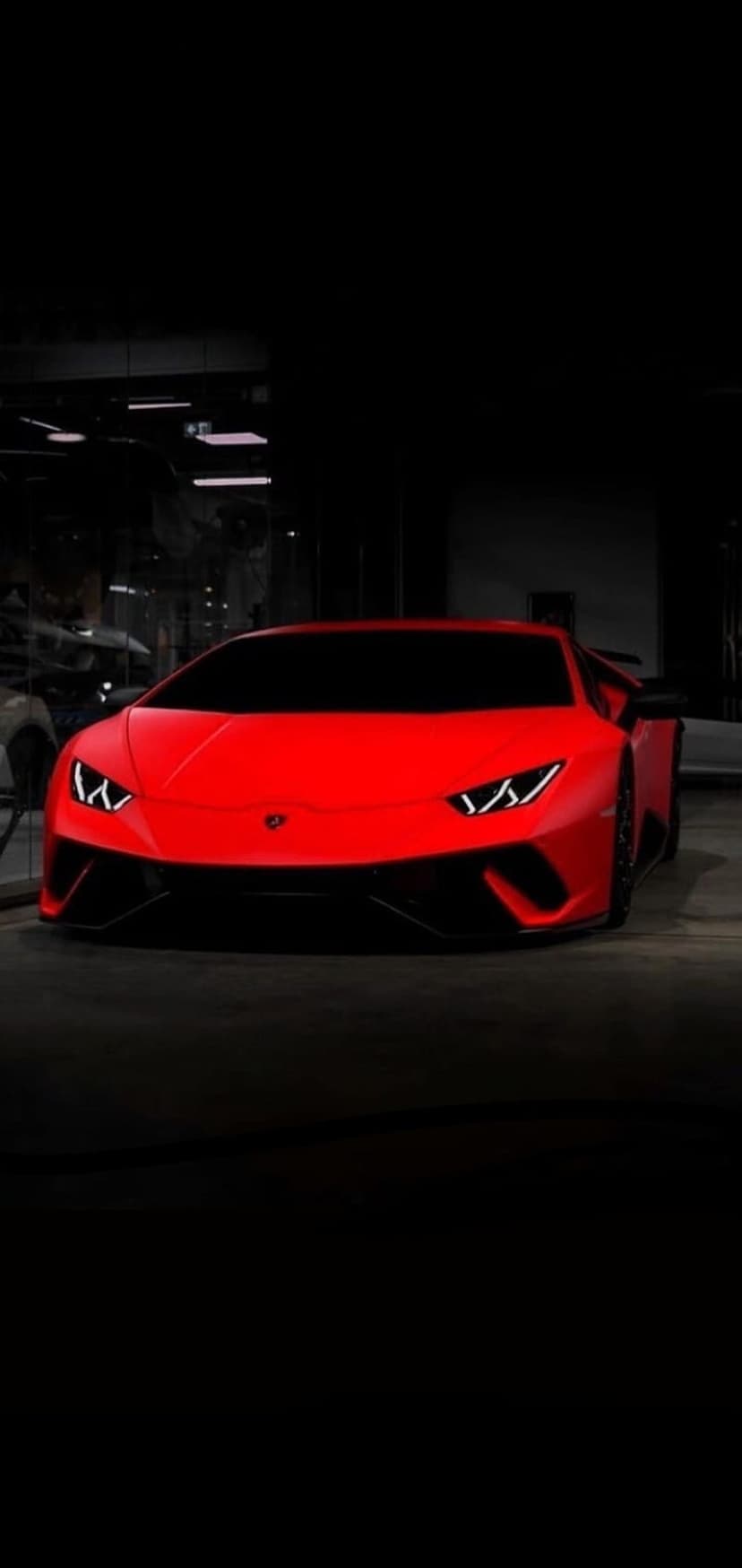 Red Lamborghini Huracan supercar in a dark showroom with glowing LED headlights and sharp aerodynamic body lines.