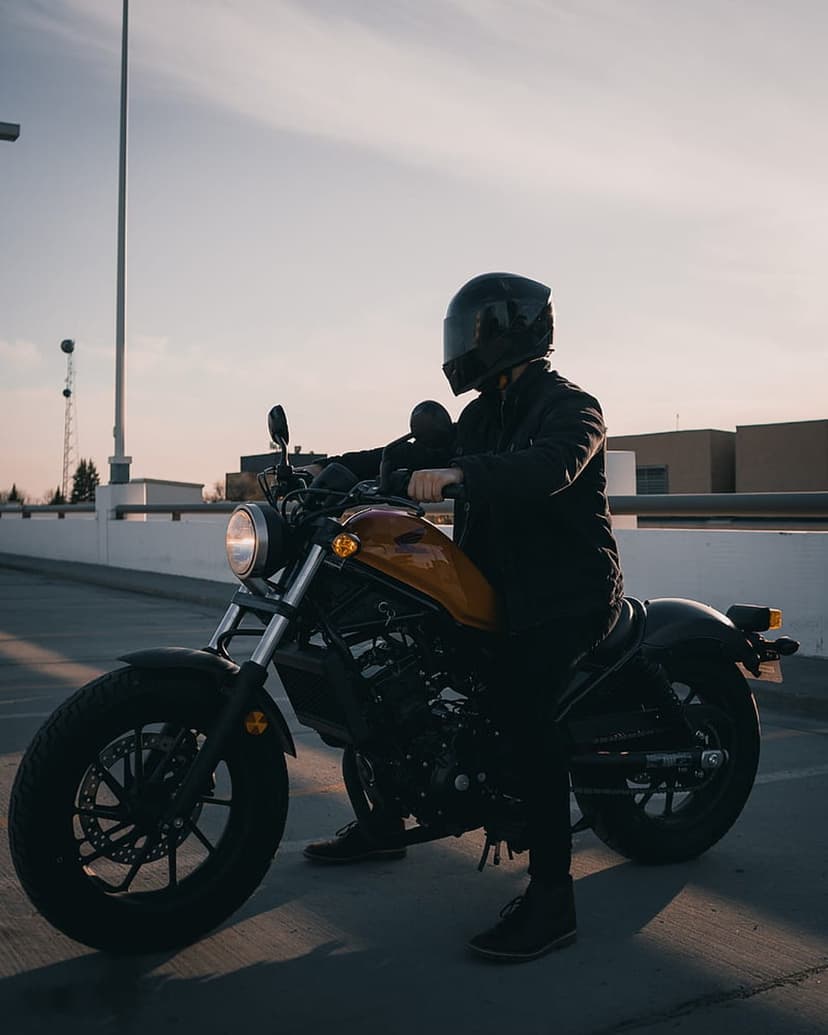 Biker in a black helmet sits on a yellow motorcycle at sunset on a parking garage deck with a clear sky background.