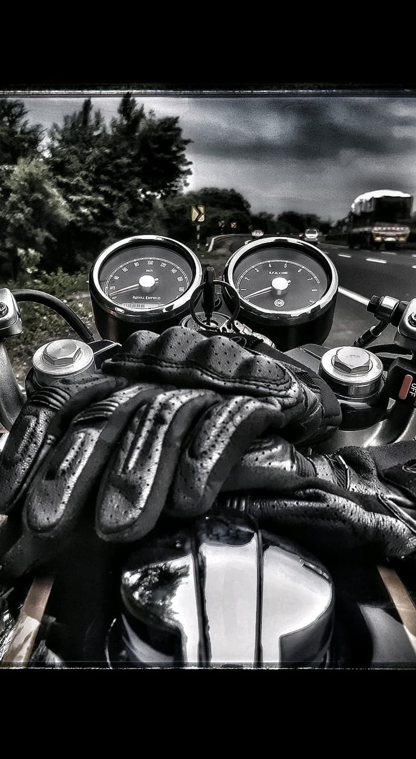 Motorcycle speedometer and tachometer next to black leather gloves on a chrome frame with a highway background.