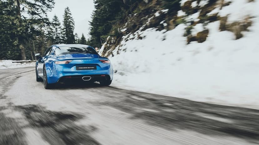 Blue Alpine A110 Premiere Edition driving fast on a snowy mountain road with dynamic motion blur effects.