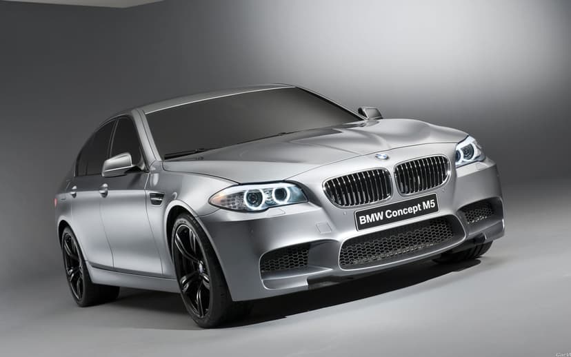 Silver BMW Concept M5 luxury sedan with glowing LED headlights in a gray studio with soft overhead lighting.