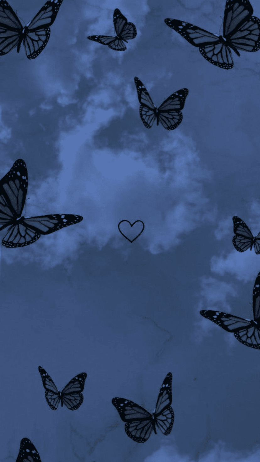 Monarch butterflies fly around a faint heart silhouette against a dark blue cloudy sky at night.