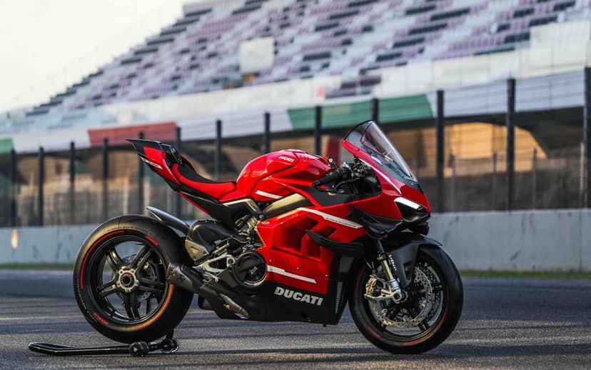 Red Ducati Superleggera V4 motorcycle parked on a race track at sunset with blurred grandstands in the background.