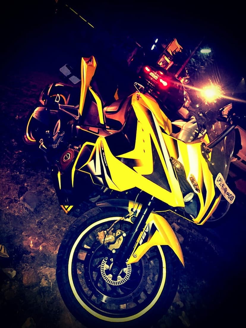 Yellow sport motorcycle with glowing headlights parked on dark ground under dramatic nocturnal lighting.