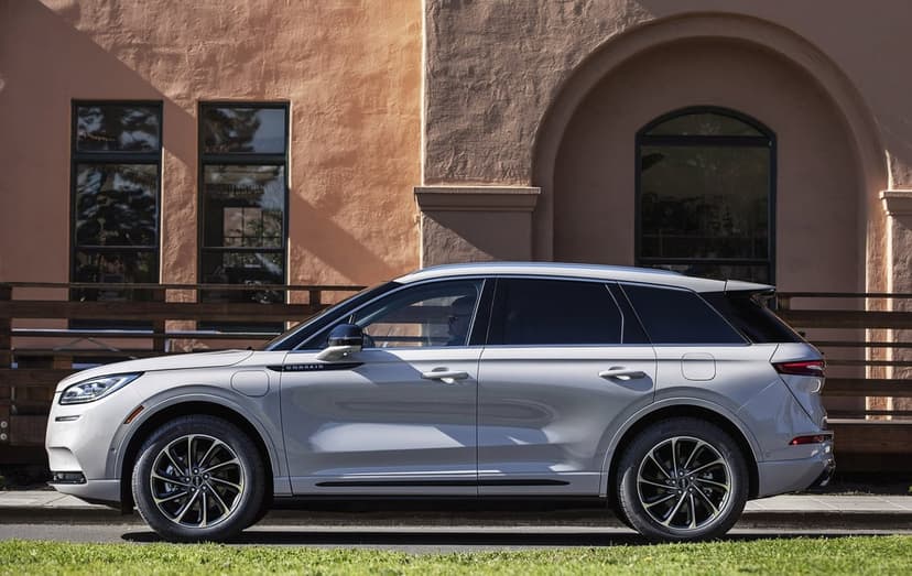 Side profile of a silver luxury SUV parked on a street against a textured peach building with arched windows.