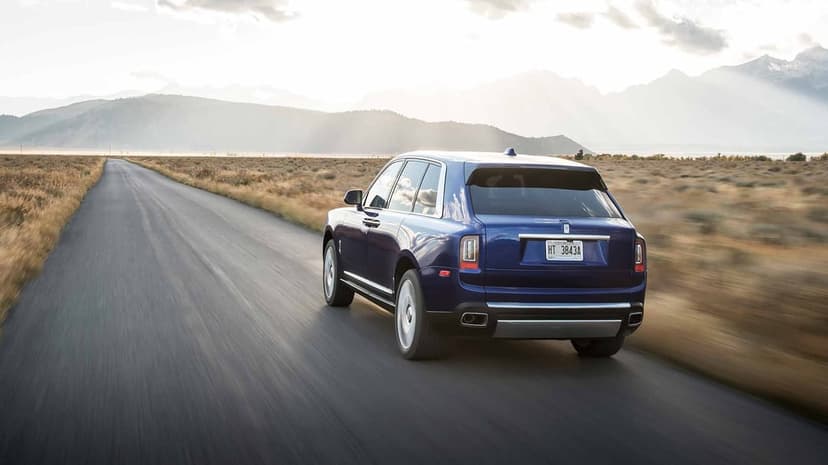 A deep blue luxury SUV driving on a straight road through golden fields toward misty mountains under a bright sky.