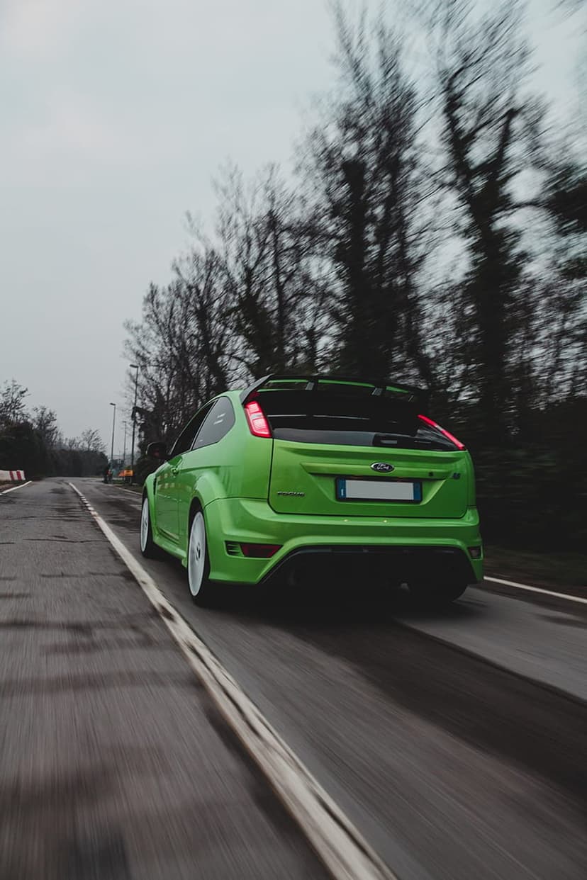 Green Ford Focus RS hatchback racing on wet asphalt with glowing red taillights and a large rear spoiler.