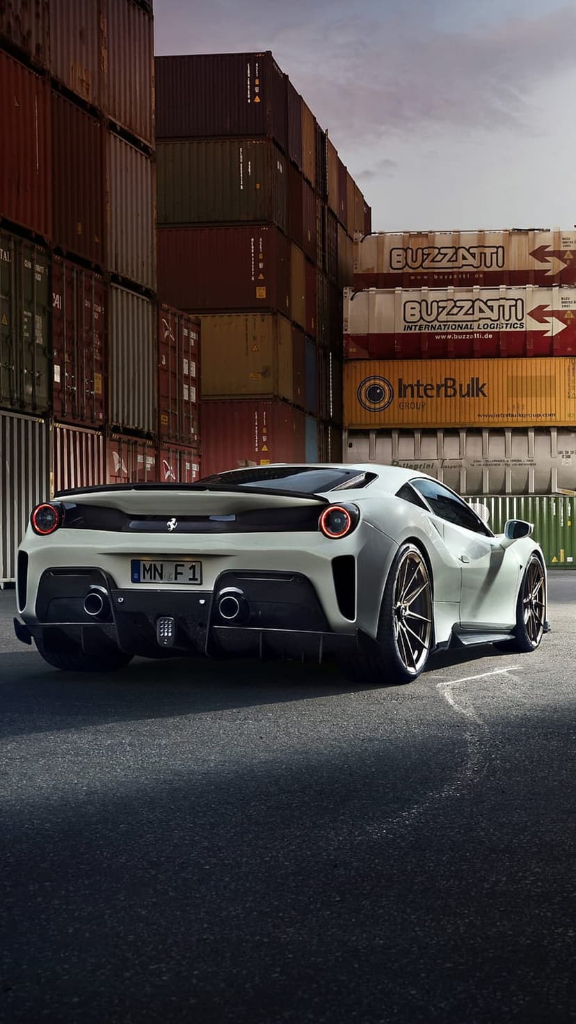 White Ferrari 458 Italia rear view parked on asphalt surrounded by colorful shipping containers in a cargo yard.