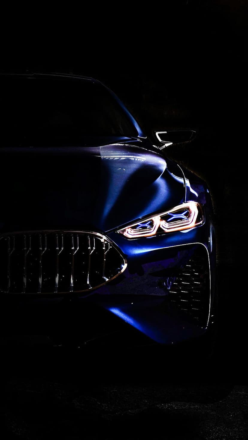 Illuminated BMW LED headlights and vertical front grille slats glowing against a dark blue metallic car body.