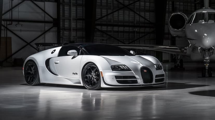 White Bugatti Veyron Super Sport and a private jet in a dimly lit industrial hangar with dramatic lighting.
