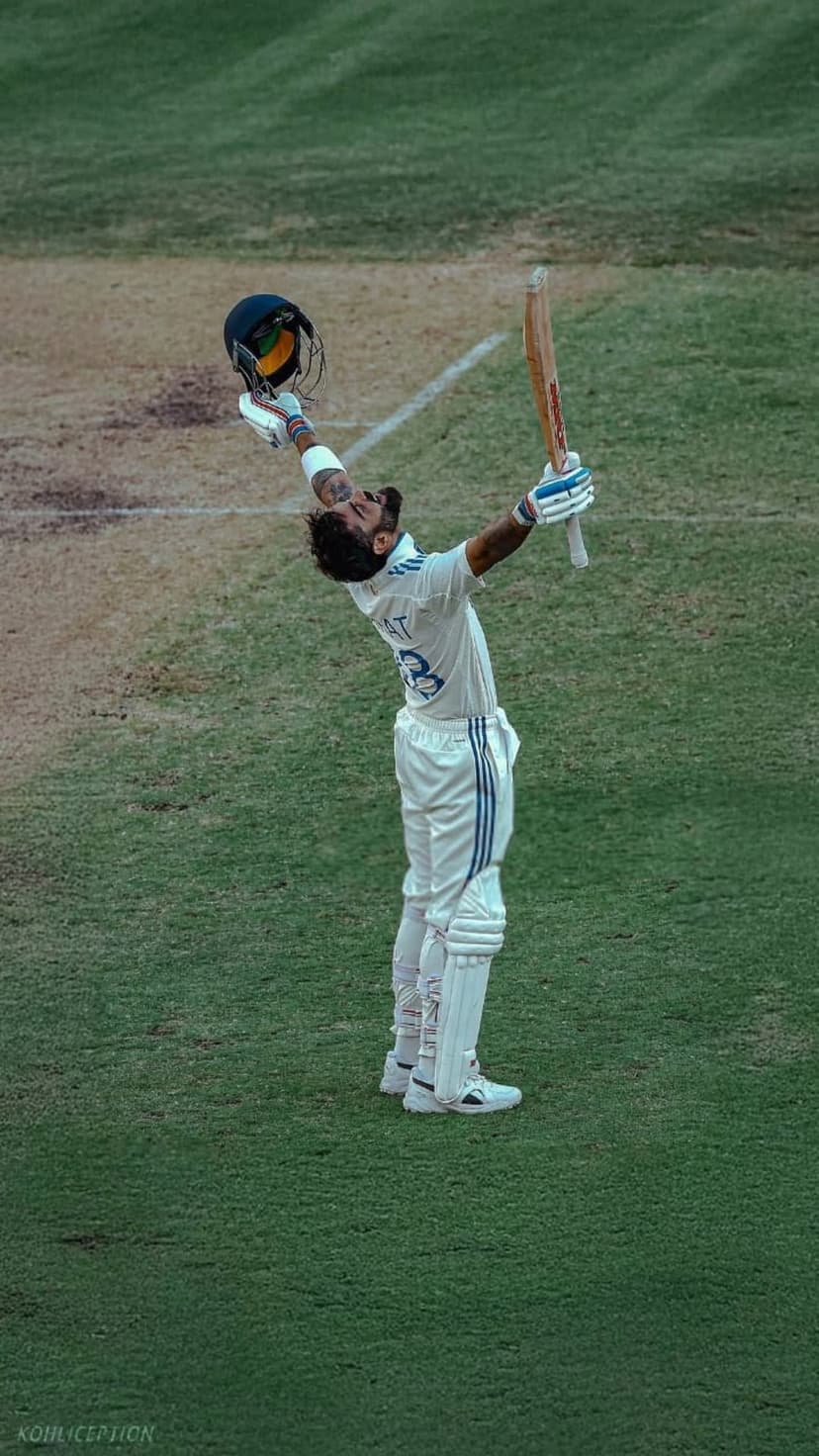 Cricket player in white raising his bat and helmet on a sunny green field during a stadium match celebration.