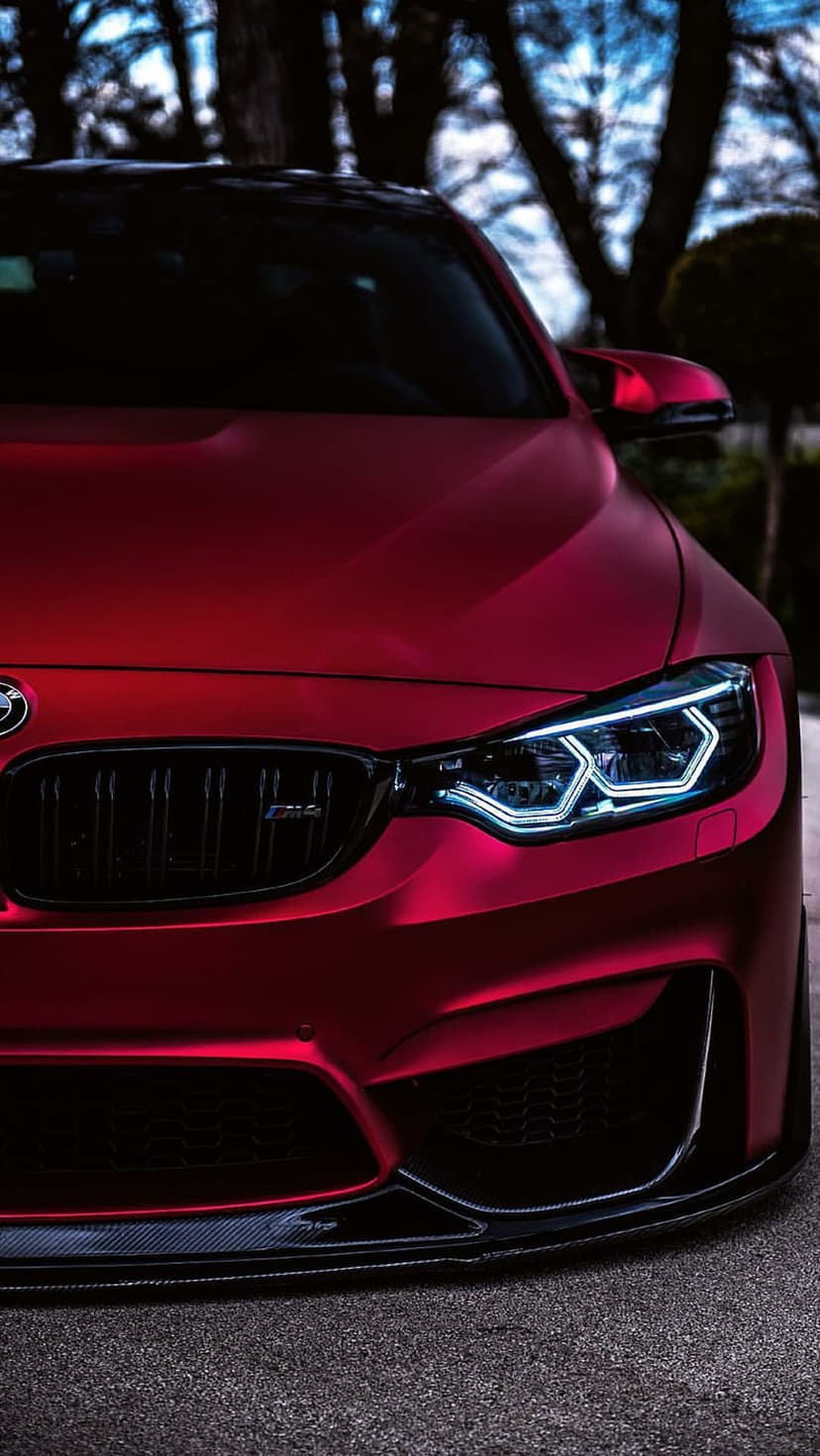 Red BMW M4 Coupe front end showing hexagonal LED headlights, a black kidney grille, and matte paint finish.
