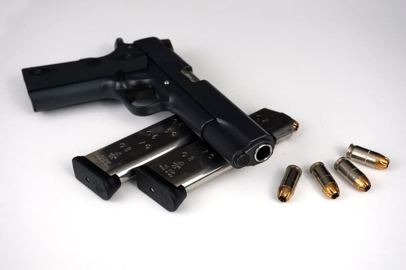 Black semi-automatic handgun lies on a white surface next to two loaded magazines and several brass bullets.