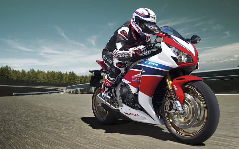 Honda CBR Fireblade sports bike with rider in HRC colors speeding through a curved road with motion blur.