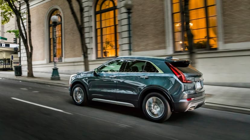 Dark teal Cadillac XT4 luxury SUV in motion on a city street beside a building with glowing arched windows.