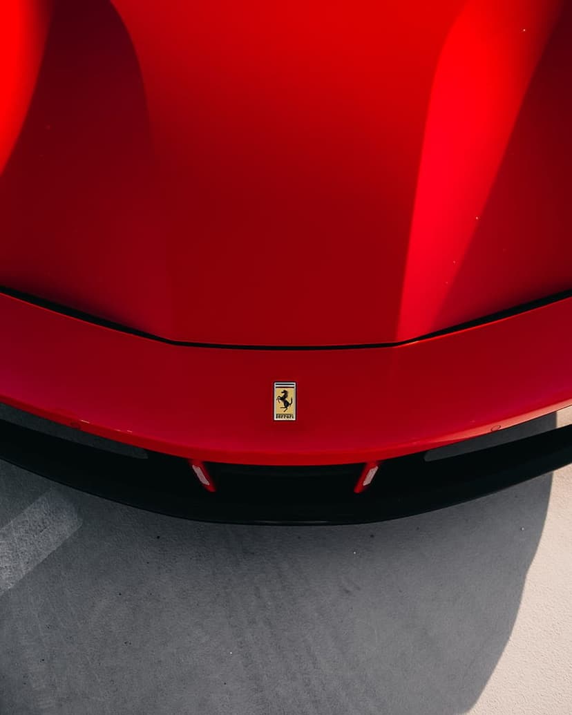 Ferrari Prancing Horse crest centered on a vibrant red metallic car hood with sunlight reflecting on the paint.
